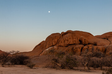 A bright moon over orange rocks. Sunset in the namibian desert, near Spitzkoppe.