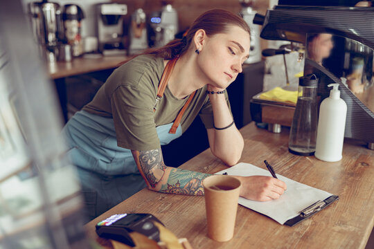 Tired female barista writing on clipboard in cafe