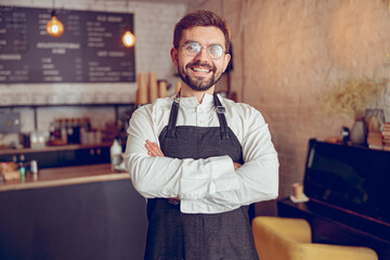 Cheerful male barista in apron standing in cafe