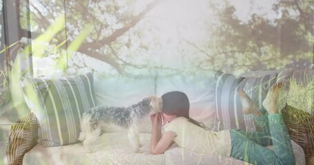Composite video of tall trees in the forest against caucasian girl playing with her dog on the couch