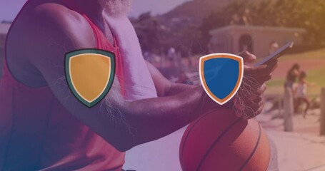 Two logo clashing against african american senior man with basketball using smartphone