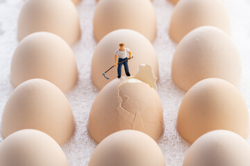 miniature man holding a sickle to crack eggshell.