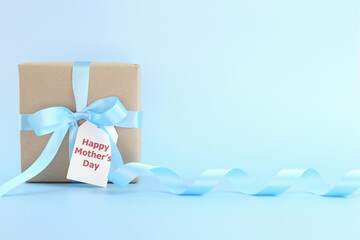 Mother's day background. Closed up brown gift box with blue bows - long ribbon and card on pastel...
