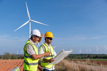 Engineer wearing uniform ,helmet hold document inspection work in wind turbine farms rotation to generate electricity energy. Green ecological power energy generation wind sustainable energy concept.