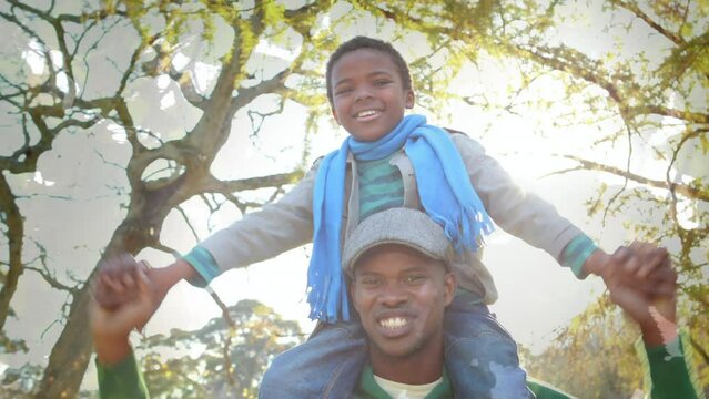 Animation of foliage over happy african american father and son having fun outdoors