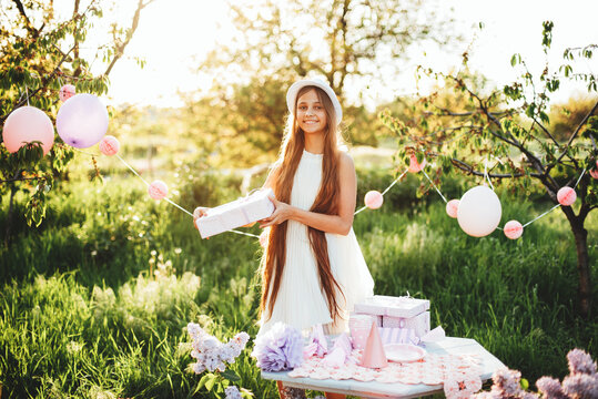 Happy birthday little girl with gift box in beautiful garden. child eat happy birthday rose cupcake. colorful pastel decoration outdoor. 13 years old kid celebrating enjoying party on summer day.