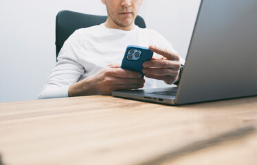 Man addicted to his phone surfing the social media on his phone while must works with his laptop