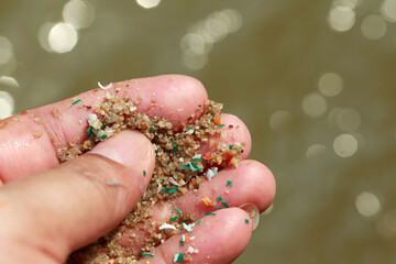 Close-up side shot of hands shows microplastic waste contaminated with the seaside sand....