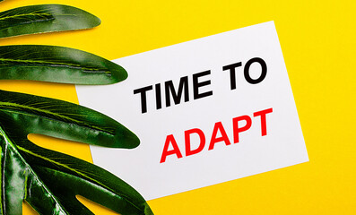 White sheet of paper with the inscription TIME TO ADAPT on a bright yellow background near the...