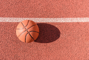 Old orange ball for basketball lying on the rubber sport court.Sport red ground outdoor in the...