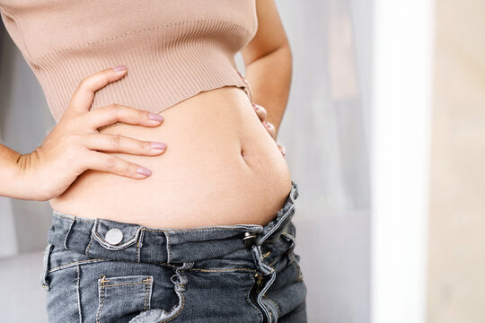 closeup belly fat woman checking her body in front of a mirror wearing jeans