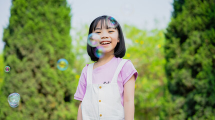 Image of Asian little girl playing with soap bubbles at park