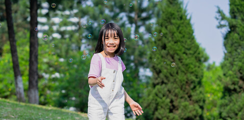 Image of Asian little girl playing with soap bubbles at park