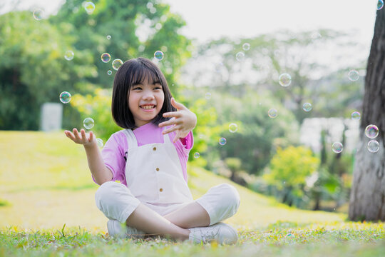 Image of Asian little girl playing with soap bubbles at park