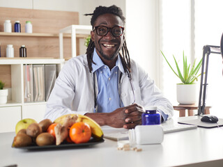 Afroamerican nutritionist looking at camera and showing healthy fruits in the consultation.