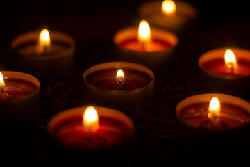 Candles burn in dark. Round candles with liquid wax and wick. Lights are orange.