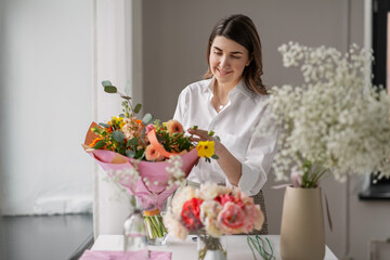 people, gardening and floral design concept - happy woman or floral artist arranging flowers in vase at home