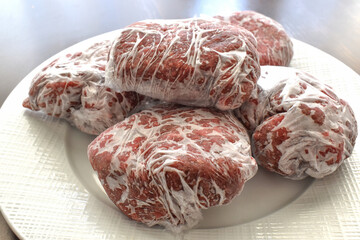 Frozen minced beef in food plastic wrap or cling film on a white plate.  Photo can be used for how...