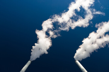 factory pipes against the blue sky. white smoke comes out of metal pipes.