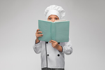 cooking, culinary and profession concept - little girl in chef's toque and jacket reading cook book over grey background - obrazy, fototapety, plakaty