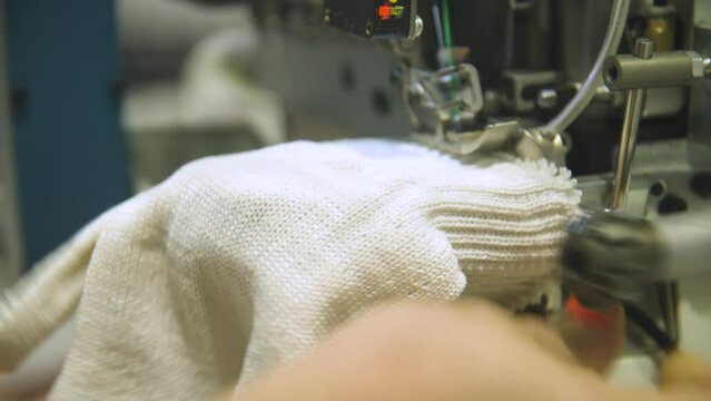 Close-up of overlock foot and cutter overlocking cuff in glove manufacturing. . The overlock machine trims the edges of the fabric. garment factory