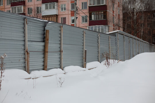 Construction site fence littered with snow. Construction site fencing in Russia. Tin fencing of an abandoned area.