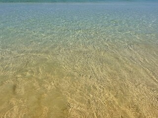 Sea coast, sandy beach. Transparent water and sand on the bottom. Sallow water, low tide. Closeup, macro view of ocean shore. Ripple on the surface. Beautiful background. Stylish backdrop. Travel idea