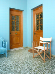Bright blue painted house entrance with two brown doors and two chairs, Chora town, Andros island, Greece.