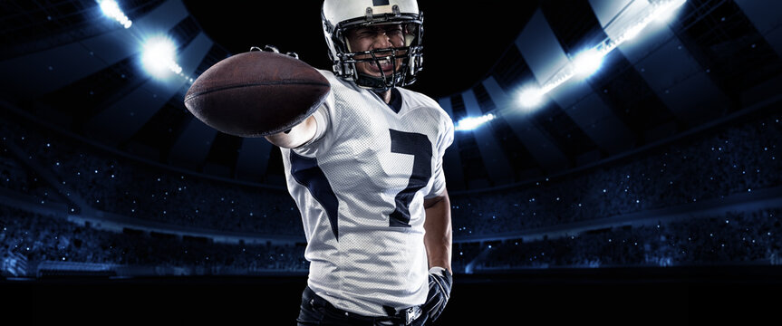 Poster with excited american football player in sports equipment holding the ball against night stadium with spotlights background. Winner emotions
