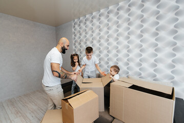 A young father with children unpacks a box of things after moving to a new apartment. Purchase of real estate. Housewarming, delivery and transportation of goods.