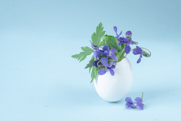 bouquet of blue flowers in a vase. Small flower arrangement. Eggshell with violets on a blue background. Easter decor and copy space