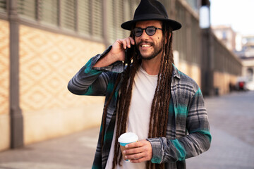Handsome guy drinking coffee while walking in the street. Modern fashion man using the phone.