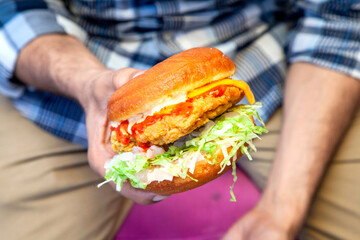 Juicy fried chicken street burger holding in one hand closeup with person in the background