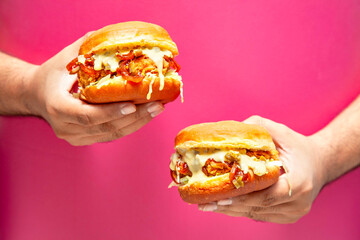 Hands holding two fried chicken on a pink coloured background.