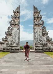 Fotobehang young male tourist wearing a traditional balinese sarong walking in front of gates of heaven temple in north bali indonesia © Alexander White