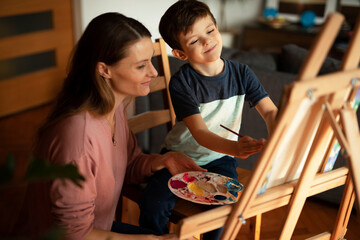 Mother and son painting at home. Little boy drawing with mom in living room