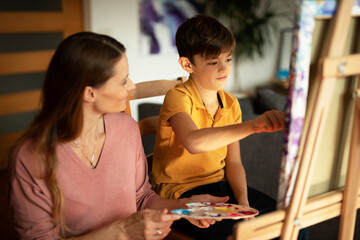 Mother and son painting at home. Little boy drawing with mom in living room
