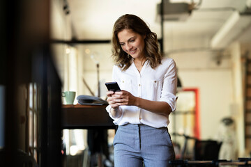 Businesswoman drinking coffee in office. Smiling businesswoman using the phone.