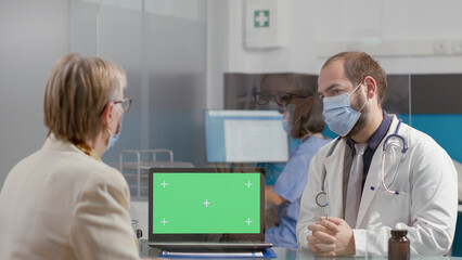 Senior woman and medic looking at greenscreen on laptop, during covid 19 pandemic. Elder patient and physician using blank chromakey template with isolated mockup background and copyspace.