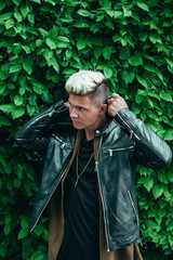 Caucasian male model with platinum blonde hair and a black leather jacket on a green leaf background