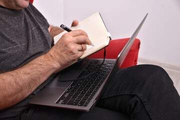 a man with a laptop on his lap taking notes in a notebook, close-up, online business analysis