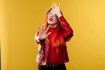Obraz premium Glamour woman wearing sunglasses in red leather jacket and with red hair posing on studio background