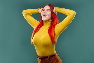 Stylish young woman with long red hair wearing yellow sweater posing emotionaly on studio background