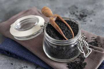 Indian spice Black cumin (nigella sativa or kalonji) seeds in glass jar with a wooden scoop close up