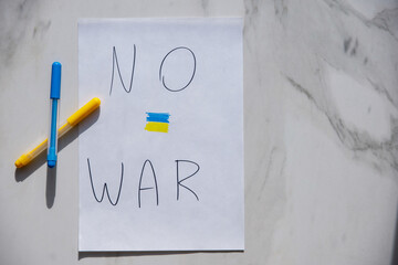 symbol of Ukraine ilosung "No War" drawn with two colored pencils on a white sheet of paper on a stone background