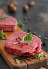 Raw beef fillet steaks with herbs and spices on wooden board on dark background close up