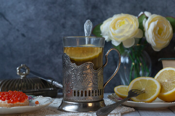 Still life in vintage style, tea with lemon in a faceted glass with a stand, caviar sandwich, sliced lemon. Still life in the style of the 40-70s.