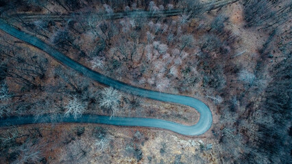Aerial high angle view of narrow winding curvy mountain road among the trees in winter forest. Bird's eye view landscape.