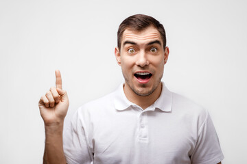 Fototapeta premium portrait of man in white T-shirt with surprised eyes. open mouth and finger points up on white background , for advertising