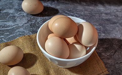 Close-up of raw chicken eggs in a white cup on a gray marble background